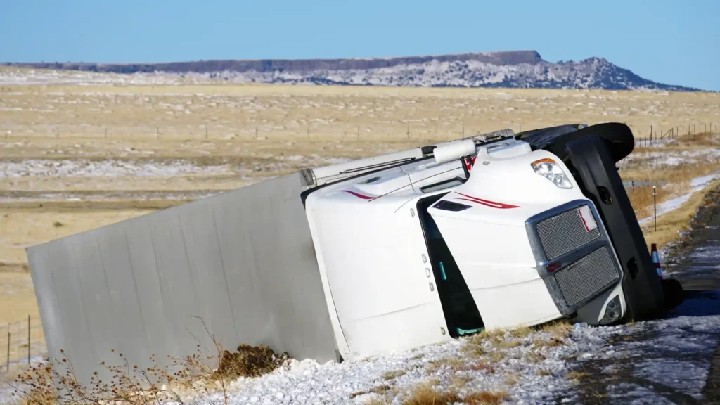 Overturned white semi-truck on the side of the road in a rural area.